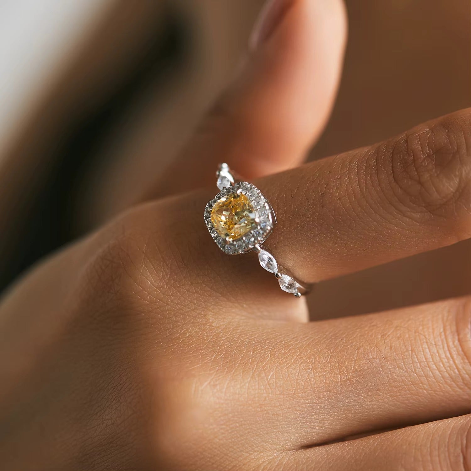 Close-up of a hand wearing a ring with a yellow gemstone on a blurred background