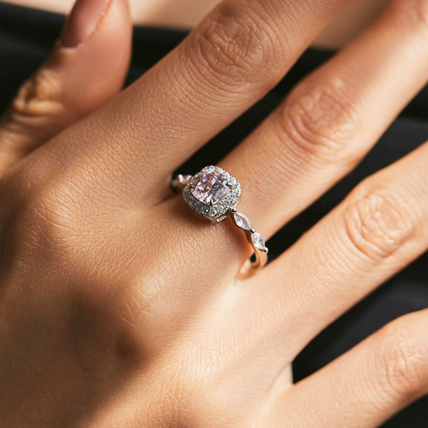 Pink diamond ring on a hand against a dark background