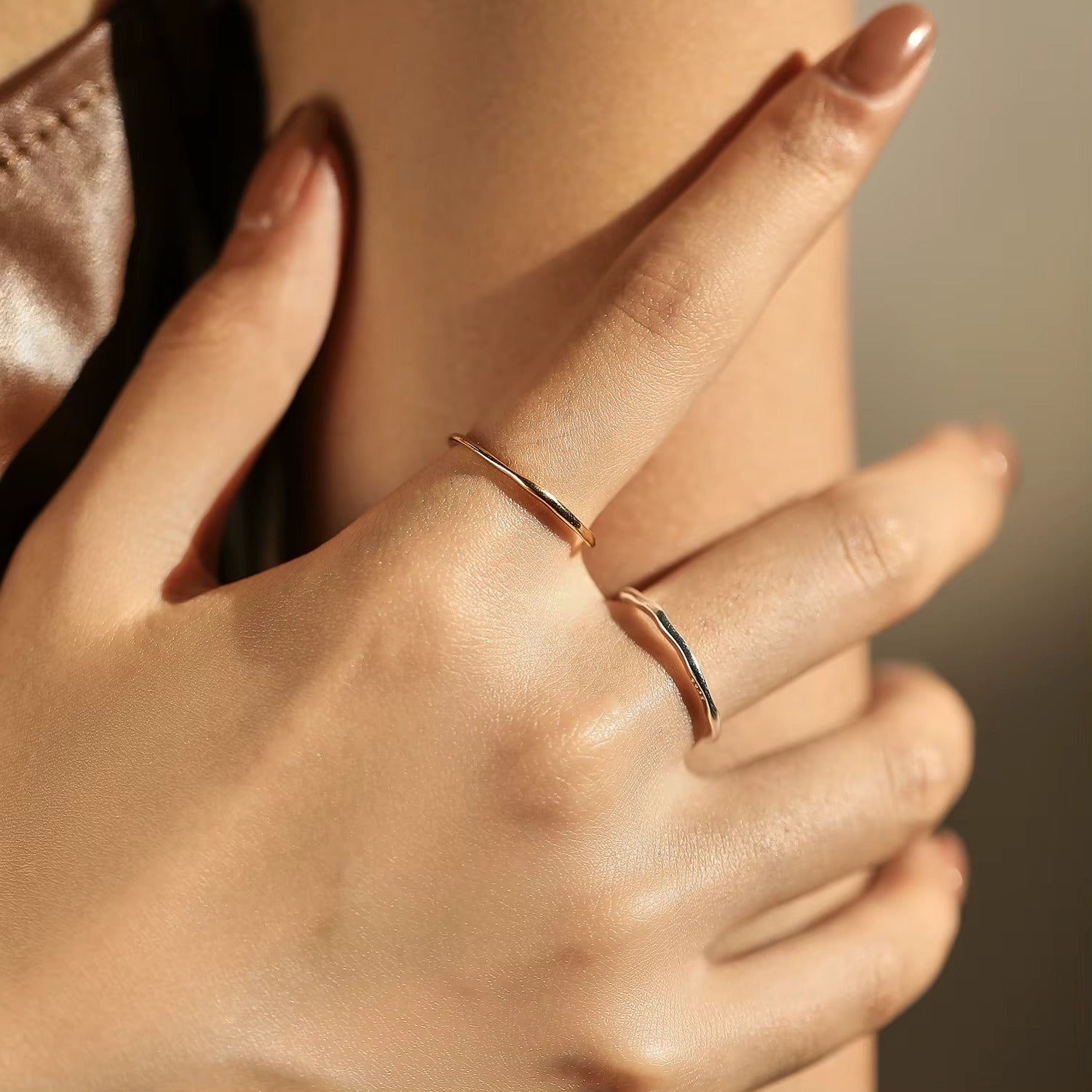 Close-up of a hand wearing two gold rings with a blurred background